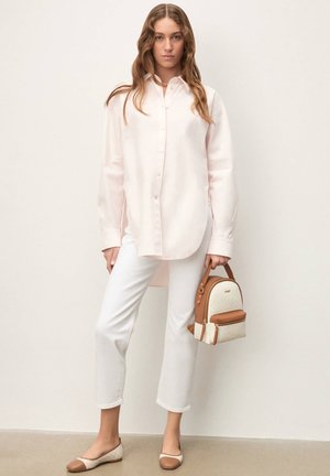 Hellrosa langärmliges Hemd, weiße Slim-Fit-Hose, beige-braune flache Schuhe und ein mini Rucksack in Hellbraun und Cremefarben. Glatte Texturen, lässiger Stil.