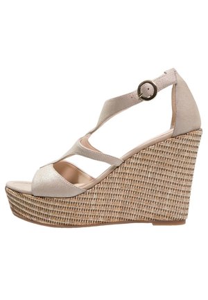 Beżowe sandały na koturnie o teksturowanej, plecionej podstawie. Posiadają krzyżujące się paski oraz zapięcie na klamrę, wykonane z miękkiego materiału syntetycznego.
