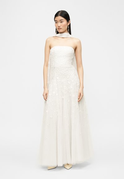 Noor naisterahvas kannab valget lillemustriga õlapaela kleiti, mille ümber on kaelas õhuke sall ning tal on pikad kõrvarõngad.