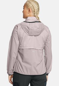 Light pink waterproof jacket with a hood, elastic cuffs, and a cropped back design. Features logo details in contrasting color.