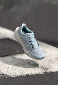 Šviesiai mėlyni sportiniai bateliai su tinklo viršumi, sustiprintu pirštu ir minkštu padu. Yra baltas vidpadis ir tekstūruotas raiščio dizainas.