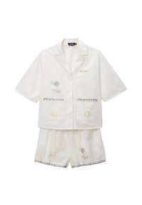 Ensemble de pyjama blanc à manches courtes avec broderie de palmiers et de soleil. Le haut possède deux poches avant ; le short présente des éléments décoratifs et des coutures similaires.