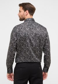 Zwarte bloempatronen blouse met lange mouwen en een spitse kraag. Bevat intrikate ontwerpen in grijstinten en beige op een zwarte achtergrond.