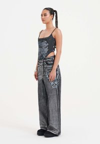 Sorte denimbukser med kraniet grafik, højtaljet, bred benpasform; parret med en tætsiddende grå tanktop med nitter og dristige tryk.