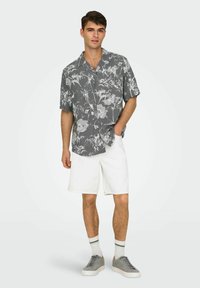 Grauhemd mit kurzen Ärmeln und weißen Blumenmustern. Kombiniert mit weißen Shorts, grauen Turnschuhen und weißen Socken mit schwarzen Streifen.