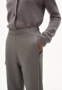Pantalon gris clair  à texture lisse, doté d'une taille haute et de poches latérales, assorti à un cardigan gris doux et duveteux.