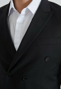 Veste de costume noire à double boutonnage avec revers en pointe, dotée d'une poche poitrine unique et de deux boutons noirs à l'avant, assortie d'une chemise habillée blanche.