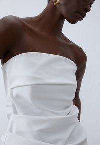 Λευκό strapless ένδυμα με εφαρμοστό κορσέ και υφασμάτινη πτύχωση γύρω από την μέση, επιδεικνύοντας λείο ύφασμα και καθαρές γραμμές.