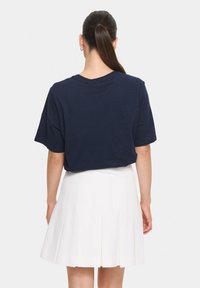 T-shirt bleu marine à manches courtes en tissu doux, associé à une jupe blanche plissée. La vue de dos montre l'ajustement décontracté du t-shirt et son encolure.