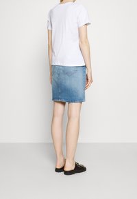 White cotton t-shirt with rolled sleeves, paired with a light blue denim skirt. The skirt features a slight fade and two back pockets. Black sandals.