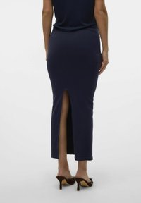 Jupe maxi côtelée bleu marine avec une fente au centre à l'arrière, design ajusté et texture lisse ; assortie avec des chaussures à talons marron.