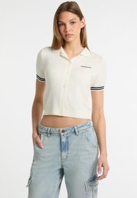 Skórzana koszulka polo w kolorze kremowym z krótkimi rękawami, z granatowymi paskami na mankietach i zapięciem na guziki, z haftowanym logo na lewej piersi.