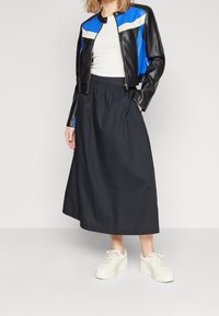 Chaqueta de cuero negra corta con detalles en azul y crema, combinada con una falda negra hasta la rodilla y zapatillas con plataforma blancas.