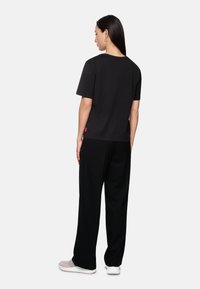 Black short-sleeve t-shirt with a round neckline, paired with black pants. Features a small logo in pink at the hem. Smooth fabric texture.