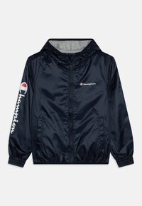 Marinblå vindjacka med huva, elastiska ärmslut, två sidofickor och Champion-logotyp på bröstet och ärmen i vitt och rött.