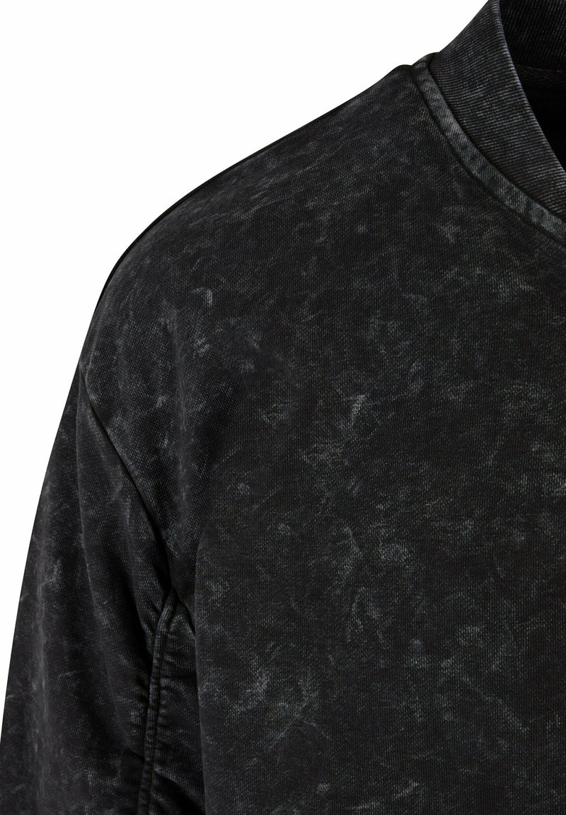 Maglione nero con un aspetto texturizzato e usurato, dotato di un collo rotondo e dettagli a coste sul colletto e sui polsini.