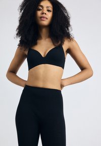 Black, seamless bra with a plunging neckline paired with high-waisted black leggings. Smooth fabric and fitted design enhance silhouette.