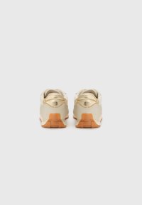 Gold sneakers with a shiny finish, rounded back, and a gum rubber sole. Detailed stitching at the heel and padded tongue for comfort.