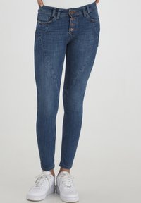 Jean skinny en denim bleu foncé, avec une taille haute, une fermeture à cinq boutons, des poches angulaires et une couture contrastante subtile.