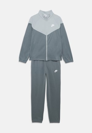 Chándal de Nike con un diseño de bloques de color en gris claro y gris oscuro. Chaqueta con cierre de cremallera y logotipo, pantalones ajustados con puños elásticos.