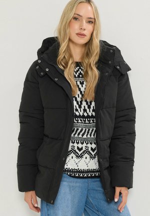 Sort puffers jakke med hætte, der har trykknapper, en quiltet design og en blød tekstur. Båret over en sweater med sort-hvidt mønster.