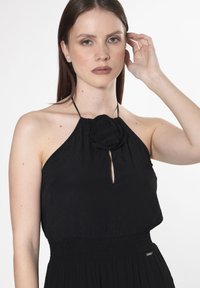 Schwarzes Halterneck-Kleid aus strukturiertem Stoff, mit einem Rosendetail am Ausschnitt und einem Schlüsselloch-Ausschnitt. Design mit gerafftem Taillenbereich.