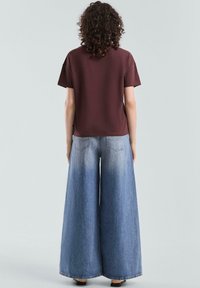 Bordeauxrotem Kurzarmhemd kombiniert mit weit geschnittenen, hellblauen Denim-Hosen, die eine hohe Taille und eine subtile Gradient-Wäsche aufweisen.