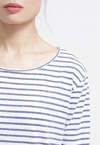 Camicia di cotone a righe con strisce orizzontali blu e bianche, dotata di un collo ampio e di una texture morbida. Primo piano del collo e delle spalle.