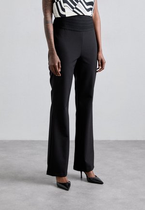 Black wide-leg pants with a smooth texture and wide waistband, paired with pointed black heels, showcasing a modern, tailored silhouette.