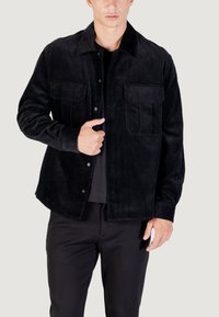 Camicia giacca in corduroy nera con colletto, due tasche sul petto e chiusura con bottoni. Presenta una texture a coste e una vestibilità rilassata.