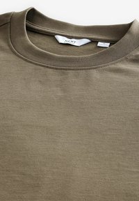 Camiseta color caqui, material de algodón, cuello redondo, mangas cortas, textura suave, diseño minimalista, presenta etiqueta de la marca en el interior del cuello.