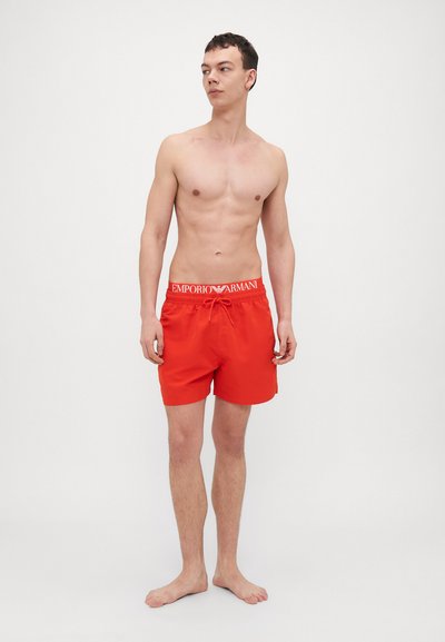 Červené plavky s elastickým pásom, na ktorom je biele logo "Emporio Armani". Hladký povrch a detail sťahovacej šnúrky.