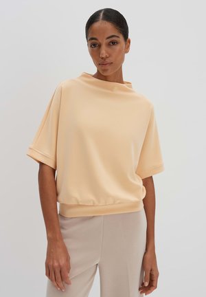 Short-sleeve, peach-colored top with a high neckline and elastic hem. Smooth fabric with a relaxed fit, complemented by wide sleeves.