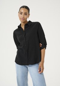 Chemise noire à boutons, fabriquée en tissu léger, dotée d'un col, de manches longues avec un détail à rabat, et d'une coupe décontractée.