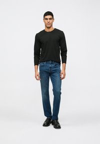 Μαύρη μακρυμάνικη μπλούζα, μπλε τζιν και μαύρα παπούτσια σε αρσενικό μοντέλο· χαλαρός στυλ, λεία υφή και κλασικά στοιχεία σχεδίασης.