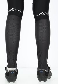 Black cycling tights with textured, hexagonal pattern sections. Features a mountain silhouette graphic at the waist and black cycling shoes.