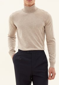 Beige rullekrave sweater lavet af blødt stof, med lange ærmer og tætsiddende design, paired med mørke bukser.