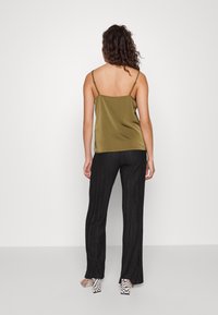 Olijfgroene satijnen camisole met dunne spaghettibandjes, gecombineerd met zwarte wijde plooibroeken, afgemaakt met gemusterde hoge hakken.