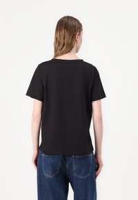 Black short-sleeved t-shirt with a round neckline, featuring a relaxed fit and a smooth texture, paired with blue denim trousers.