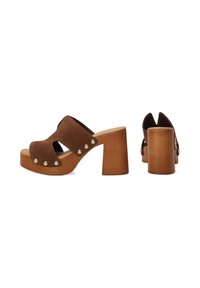 Bruine suède open-toe mules met een brede band, houten blokhak, gouden studs langs de zijkant en een gebogen uitsnijdingsontwerp.