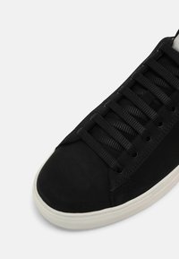 Baskets noires avec des lacets noirs et une semelle en caoutchouc blanche, vues du dessus en mettant l'accent sur la pointe et les lacets.