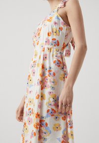 Robe midi florale en tissu léger, ornée de fleurs orange, rose et jaune sur fond blanc, avec des détails à volants aux épaules.
