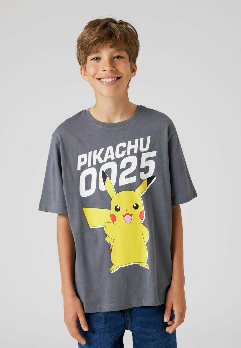 Pilka medvilninė marškinėliai su dideliu geltonu Pikachu grafinu ir tekstu "PIKACHU 0025", su laisvu kirpimu ir trumpomis rankovėmis.