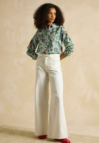 Cămașă verde cu motive, cu imprimeuri florale și grafice, asociată cu blugi largi albi cu talie înaltă și pantofi roșii.