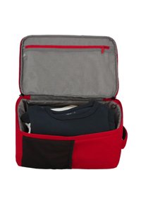 Rode reistas met een grijze binnenkant, gedeeltelijk open. Bevat opgevouwen t-shirts, met een zijvak van zwart textiel. Met een rits aan de bovenkant.