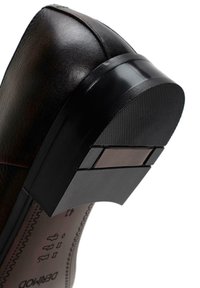 Zapato de cuero marrón con una suela de goma negra texturizada y un tacón rectangular. Presenta un acabado liso y un detalle de costura mínimo.