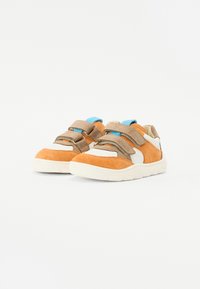 Des chaussures en daim orange et tan avec des accents crème, dotées de deux brides Velcro réglables et d'une semelle en caoutchouc texturé.