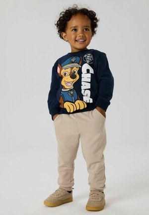 Sudadera navy con el perro caricaturesco Chase, con el texto "CHASE"; combinada con pantalones beige y zapatos marrones. Tejido suave, diseño casual.