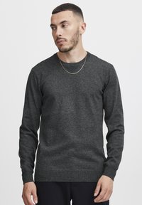 Maglione grigio a collo rotondo, tessuto lavorato a maglia, maniche lunghe, collo e orlo a coste, texture minimal, senza modelli o grafiche visibili.