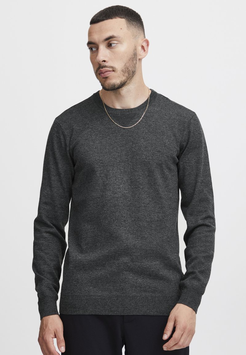 Maglione grigio a collo rotondo, tessuto lavorato a maglia, maniche lunghe, collo e orlo a coste, texture minimal, senza modelli o grafiche visibili.